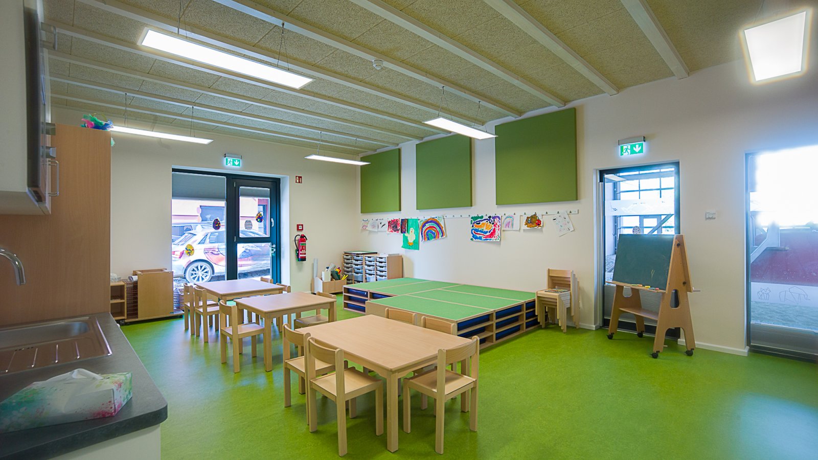 Group room of a day care centre with green floor and wooden tables and chairs